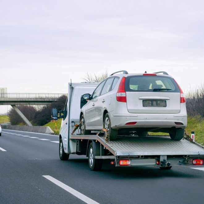 Tow truck with car on warranty on road. Trailer and crash auto delivery. Vehicles hauler on driveway. European transport logistics. Heavy haul trailer with driver on highway.